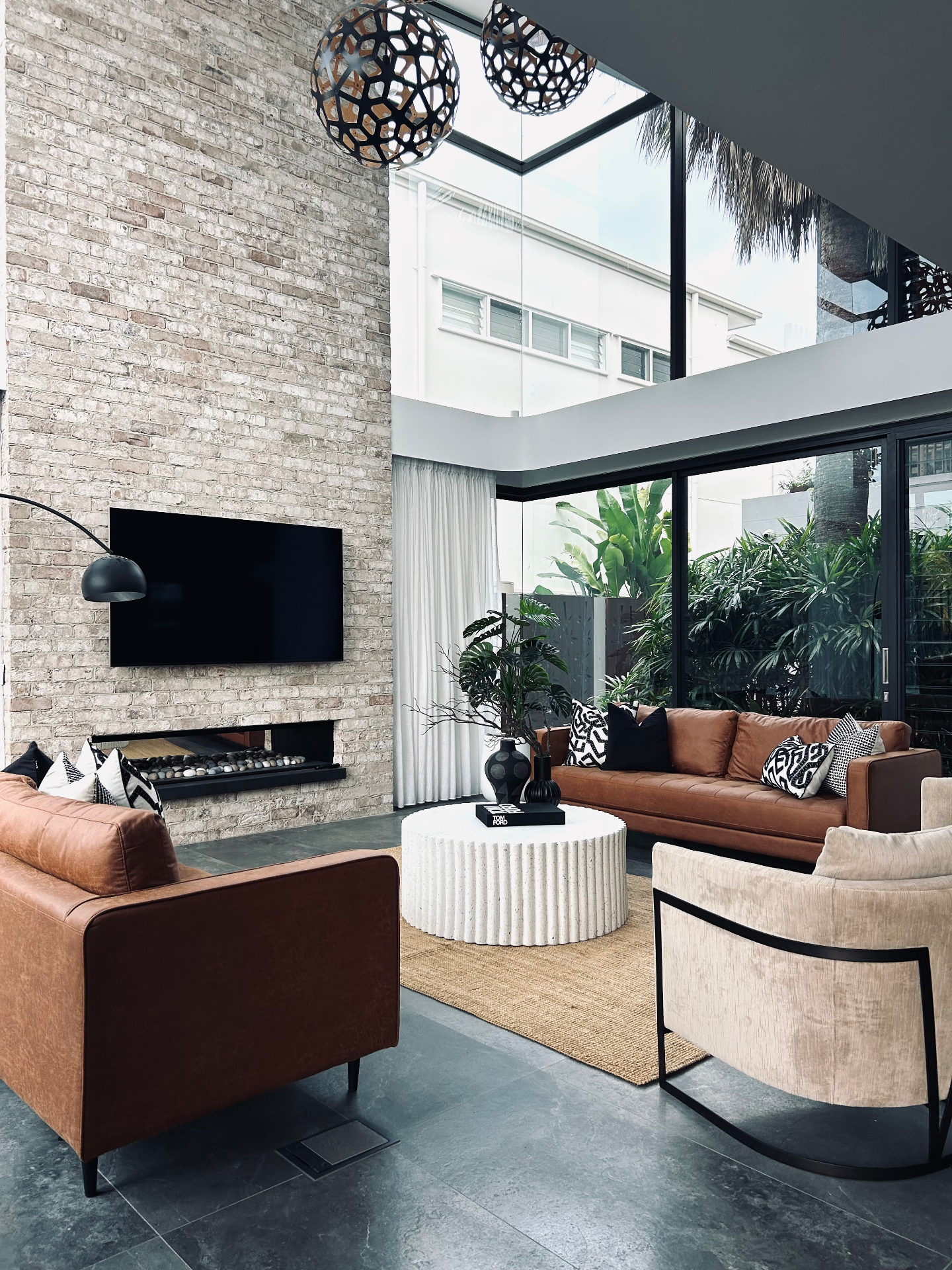 Styled Gold Coast living room with leather sofas, brick fireplace, and atrium ceiling